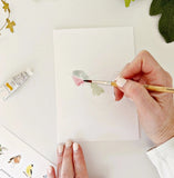 Person painting a bird design on a white sheet of paper with a brush.