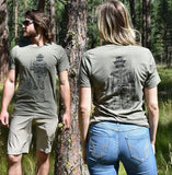 Two people wearing matching olive green t-shirts with a Smokey Bear design in a forest setting.