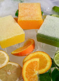 Three Scrubby soap bars surrounded by citrus fruits.