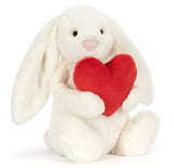 White plush bunny with big floppy ears holding a plush red heart.