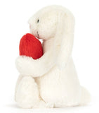 White plush bunny with big floppy ears holding a plush red heart.