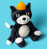 Black and white plush toy cat with an orange cap and smiling expression.