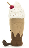Plush toy resembling a chocolate milkshake with whipped cream and a cherry on top. It has a smiling face and brown corduroy legs.