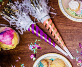 Striped party horns on table next to plates of icecream.