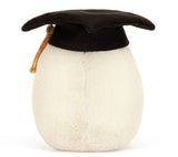 A plush toy boiled egg, wearing a graduation cap with gold tassel. It has a smiling face and brown corduroy legs.