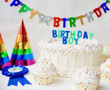 Birthday cake with 'Happy Birthday' banner, colorful party hats, and cupcakes on a white background.