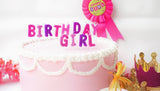 Pink birthday cake with 'Birthday Girl' text and a pink ribbon on a white background.