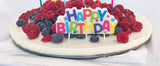 Birthday cake with berries and a colorful 'Happy Birthday' candle.