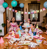Children at a birthday party with a cake and decorations in a room.