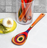 Colorful ceramic spoon on a white surface with a glass container holding additional spoons.