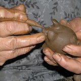 Person shaping a small clay pig with a tool.